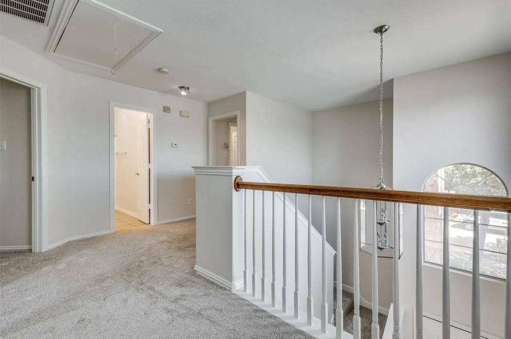 Carpeted hallway with white walls, white wood-finish railing, and an arched window