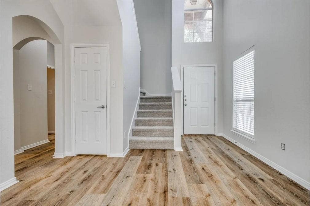 Wood-finish flooring, carpeted stairs, arched doorway, and an upper arched window