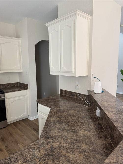 Full-height white cabinetry with crown molding, durable countertop surfaces, wood-finish flooring, and a stainless steel appliance