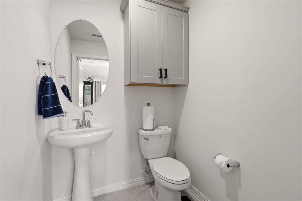 4808 Forest Crest Parkway, Arlington, TX 76005 Pedestal sink with chrome faucet, oval wall-mounted mirror, and wall-mounted cabinetry with matte black hardware