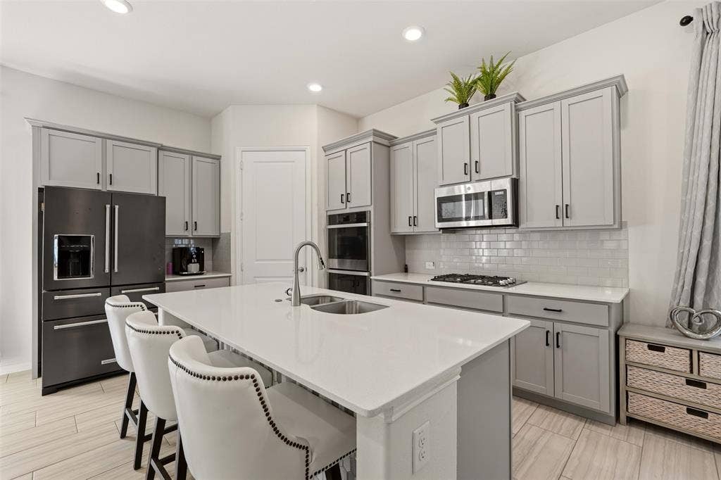 4808 Forest Crest Parkway, Arlington, TX 76005 Kitchen featuring gray shaker cabinetry, stainless steel appliances, a center island with an integrated sink, white subway tile backsplash, and wood-finish flooring