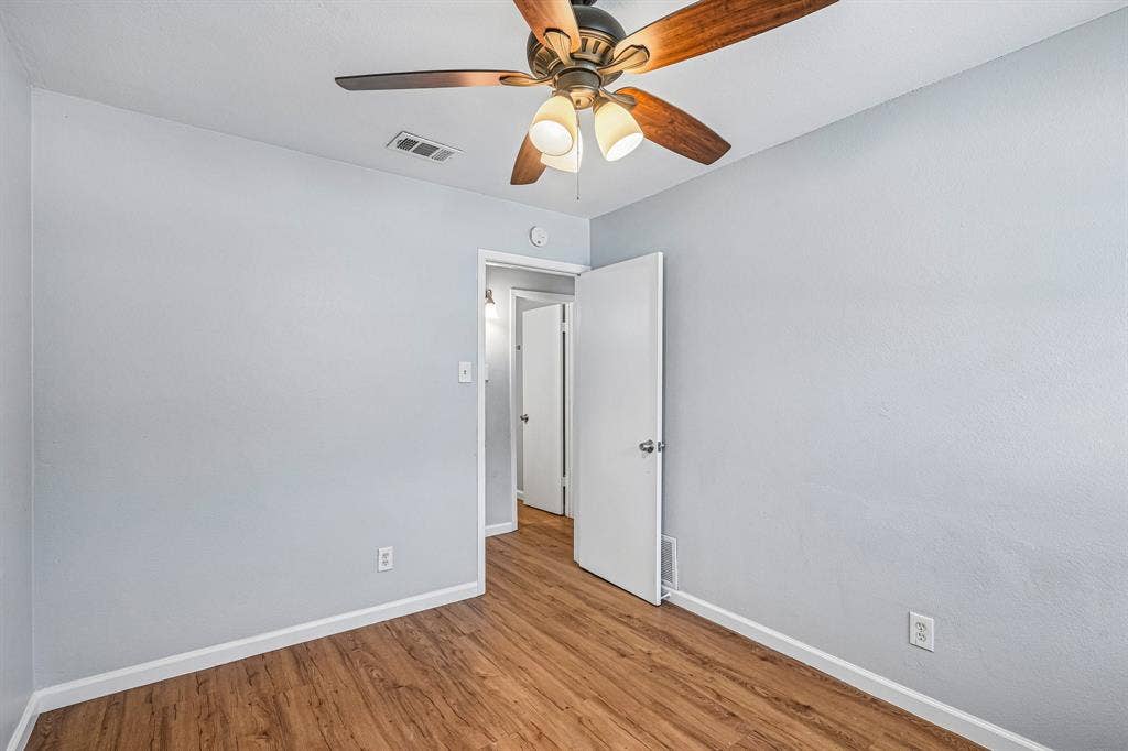 Wood-finish flooring, light blue wall paint, and a ceiling fan with integrated lighting