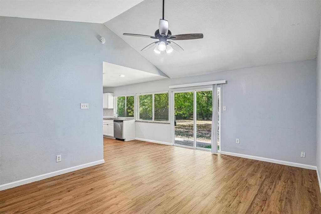 Vaulted ceiling with a ceiling fan, wood-finish flooring, sliding glass door, and white lower cabinetry with a stainless steel appliance