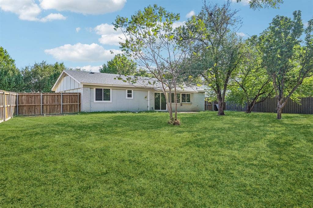 Expansive backyard featuring a lush lawn, mature trees, wood privacy fencing, and a sliding glass door
