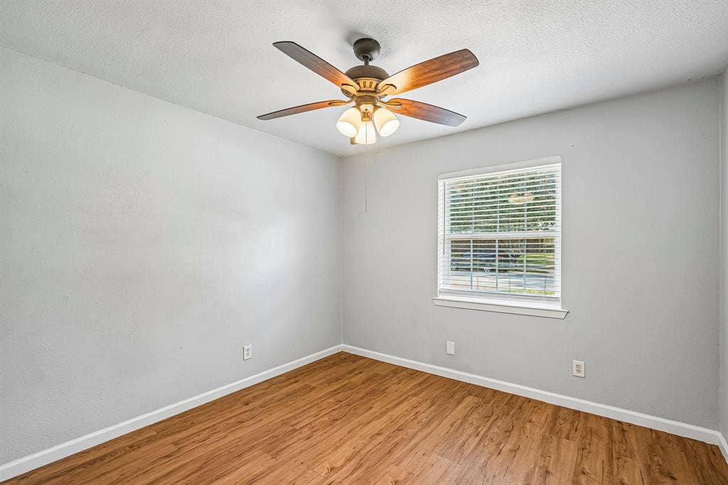 Wood-finish flooring, single window with blinds, ceiling fan with integrated lighting, light gray wall paint, and white trim