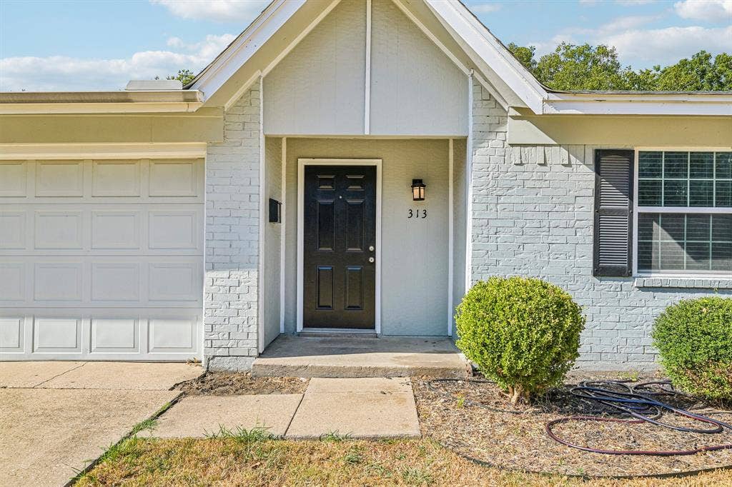 Painted brick exterior with a paneled garage door, black front door, and exterior sconce lighting