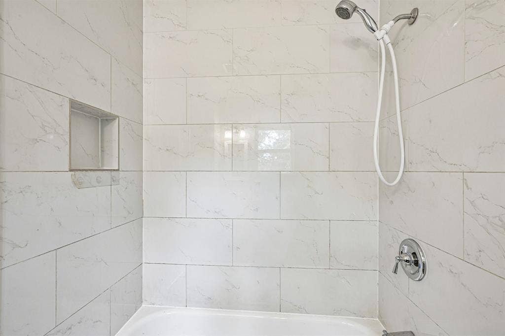 Bathtub with a chrome shower head and faucet, white subway tile surround, and a recessed shower niche