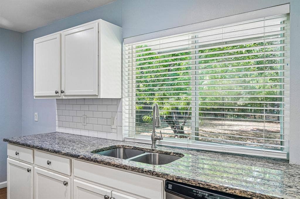 White shaker-style upper and lower cabinetry, speckled stone countertops, undermount double-basin sink with a pull-down faucet, and white subway tile backsplash