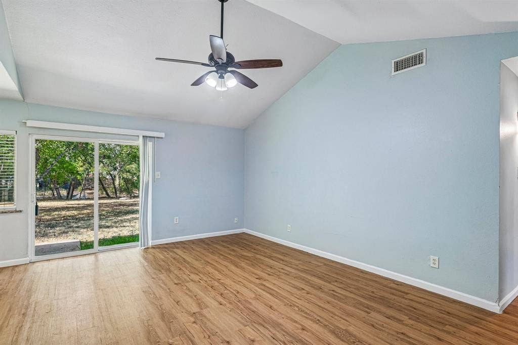 Vaulted ceiling with a ceiling fan light fixture, wood-finish flooring, and a sliding glass door providing natural illumination