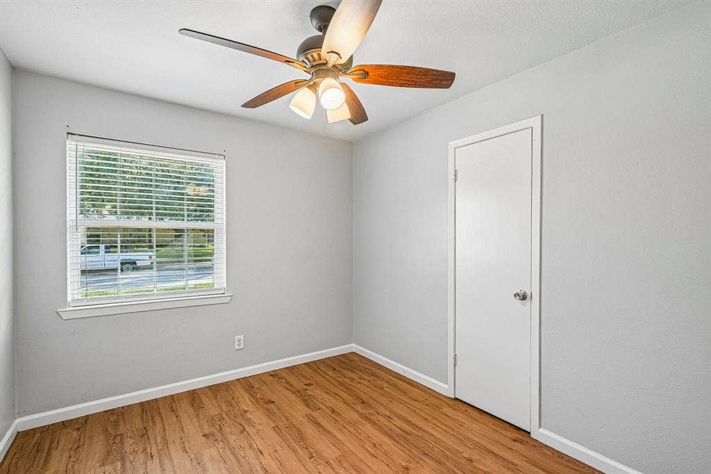Wood-finish flooring, ceiling fan with integrated lighting, window with blinds, and a white interior door