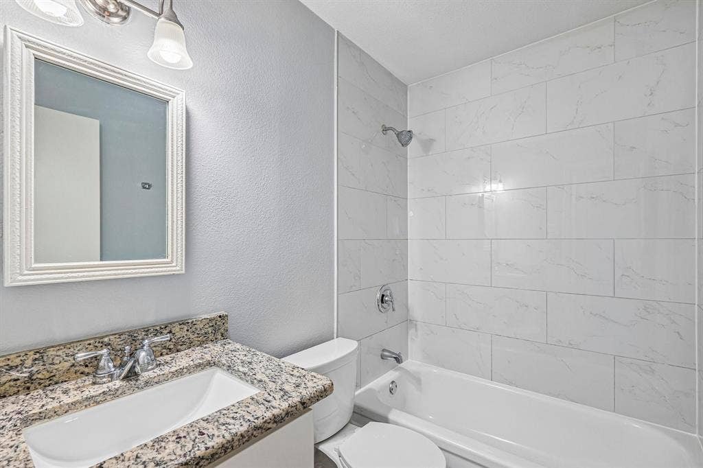 White subway tile shower surround, integrated bathtub, vanity with granite countertop, undermount sink, and chrome fixtures