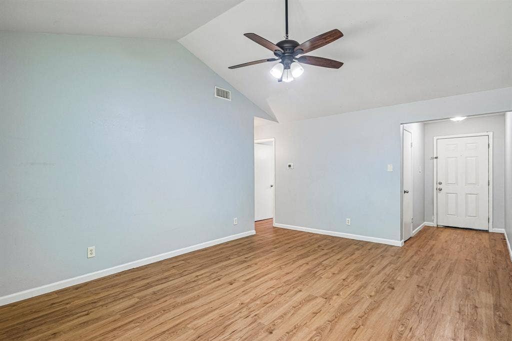 Vaulted ceiling with a ceiling fan light fixture, wood-finish flooring, and a paneled entry door