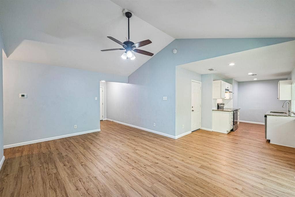 Vaulted ceiling with a ceiling fan, wood-finish flooring, white cabinetry, and stainless steel appliances