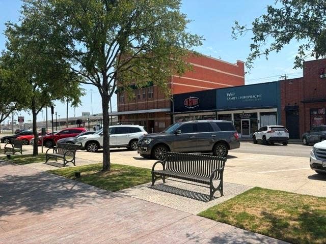1012 S Elm Street, Carrollton, TX 75006 Sidewalk area featuring mature trees, landscaped planting beds, and multiple public benches