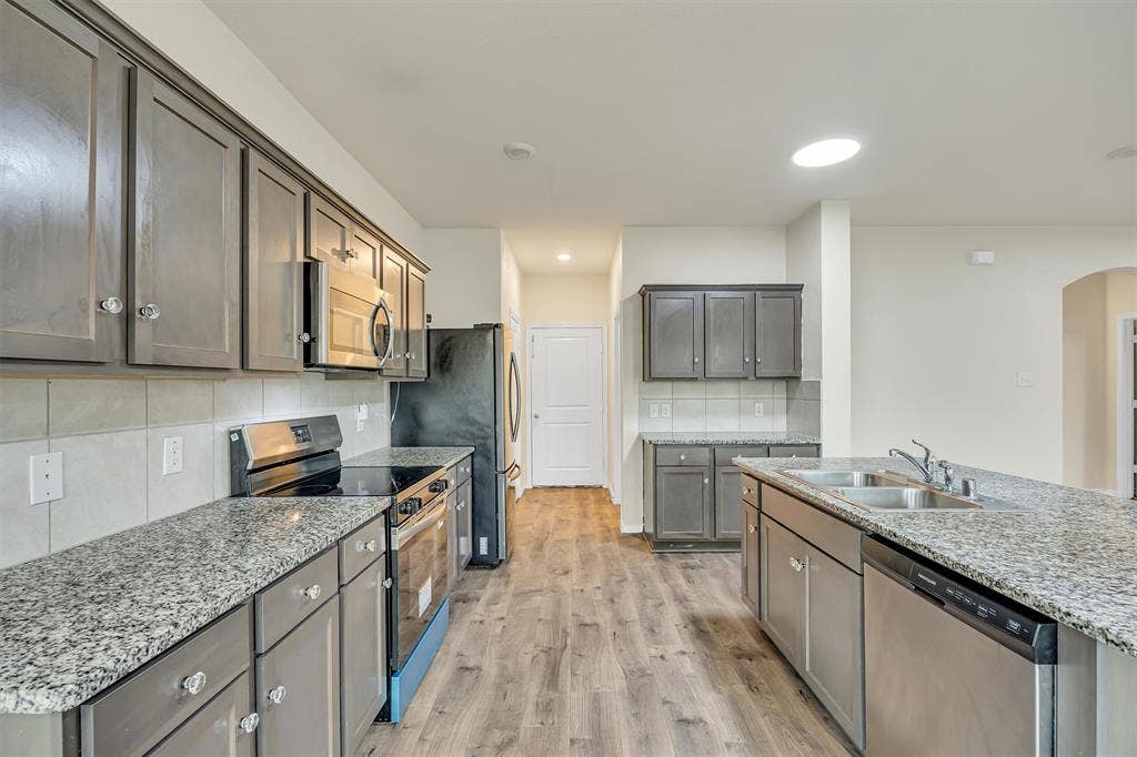 Kitchen featuring wood-finish flooring, granite countertops, gray cabinetry, stainless steel appliances, and a tiled backsplash