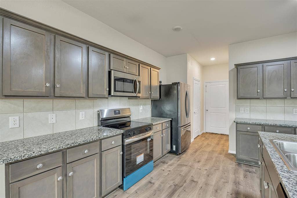 Kitchen featuring wood-finish flooring, gray cabinetry, stainless steel appliances, granite countertops, and a tile backsplash