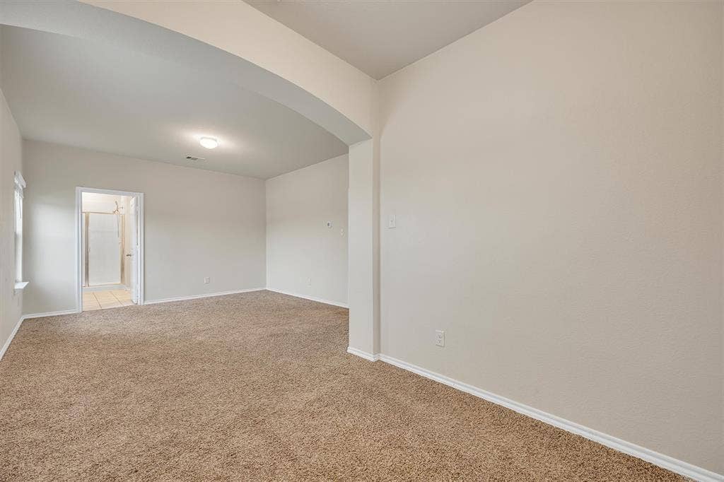 Arched entryway to a carpeted room featuring a single window, overhead lighting, and neutral wall paint