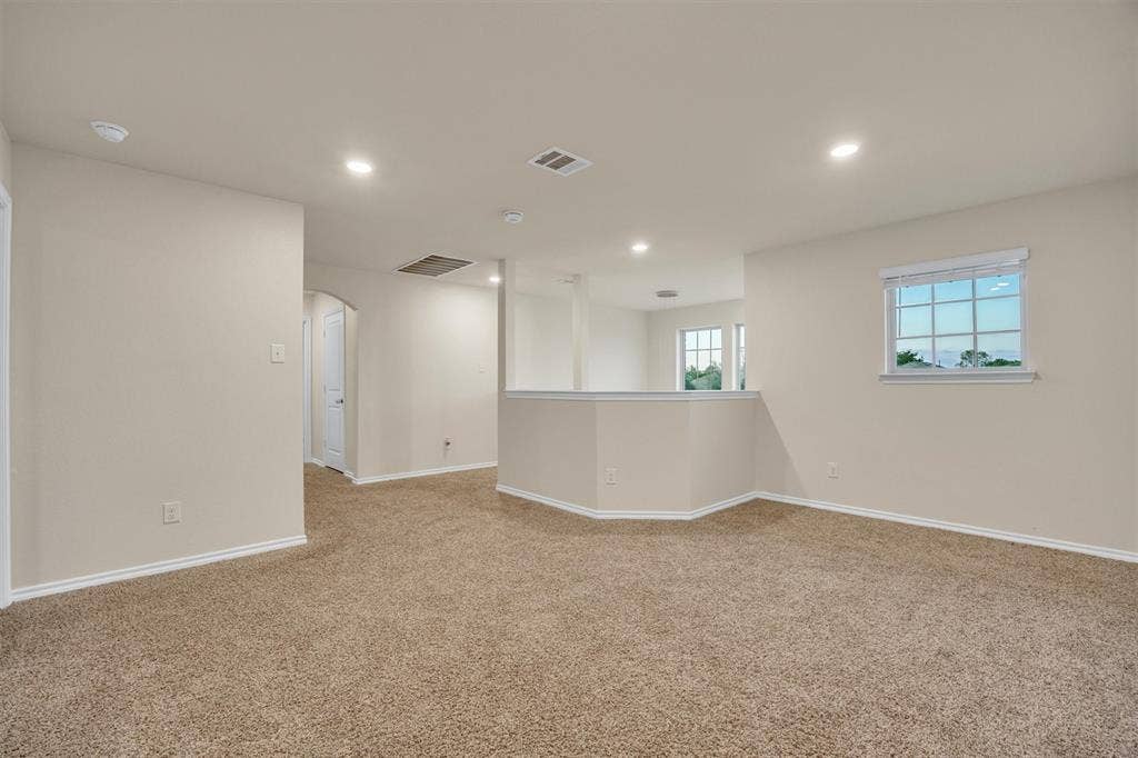 Spacious carpeted area featuring recessed lighting, a window with blinds, and a built-in half-wall partition