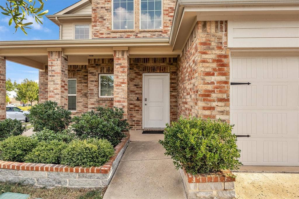 Brick exterior with an integrated garage, covered entry, and decorative shrubbery