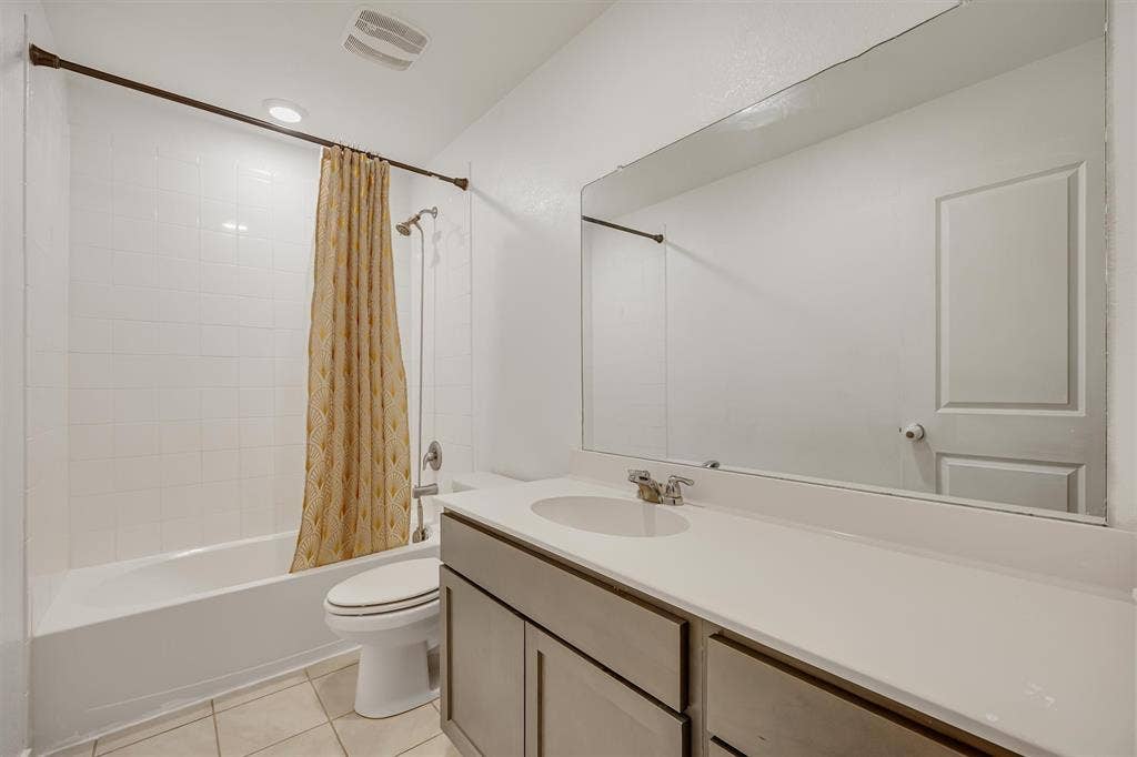 Full bathroom with a white tile shower-over-tub, extended vanity with an integrated sink, and a large wall-mounted mirror