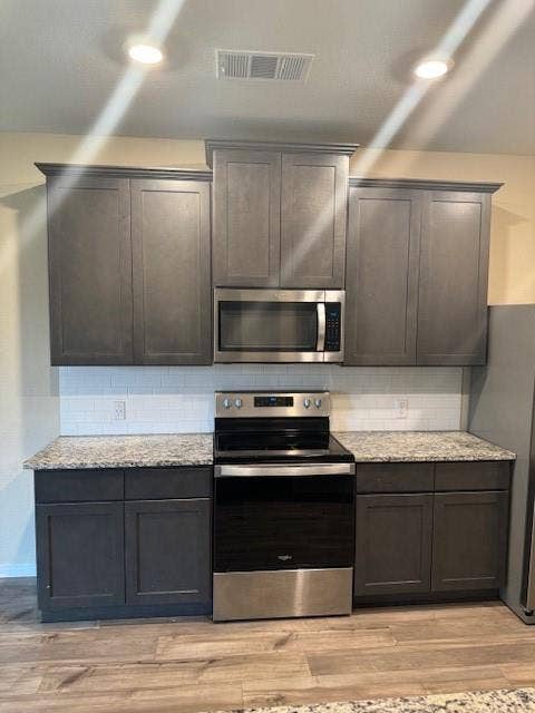 Kitchen featuring dark gray cabinetry, stainless steel appliances, granite countertops, white subway tile backsplash, and wood-finish flooring