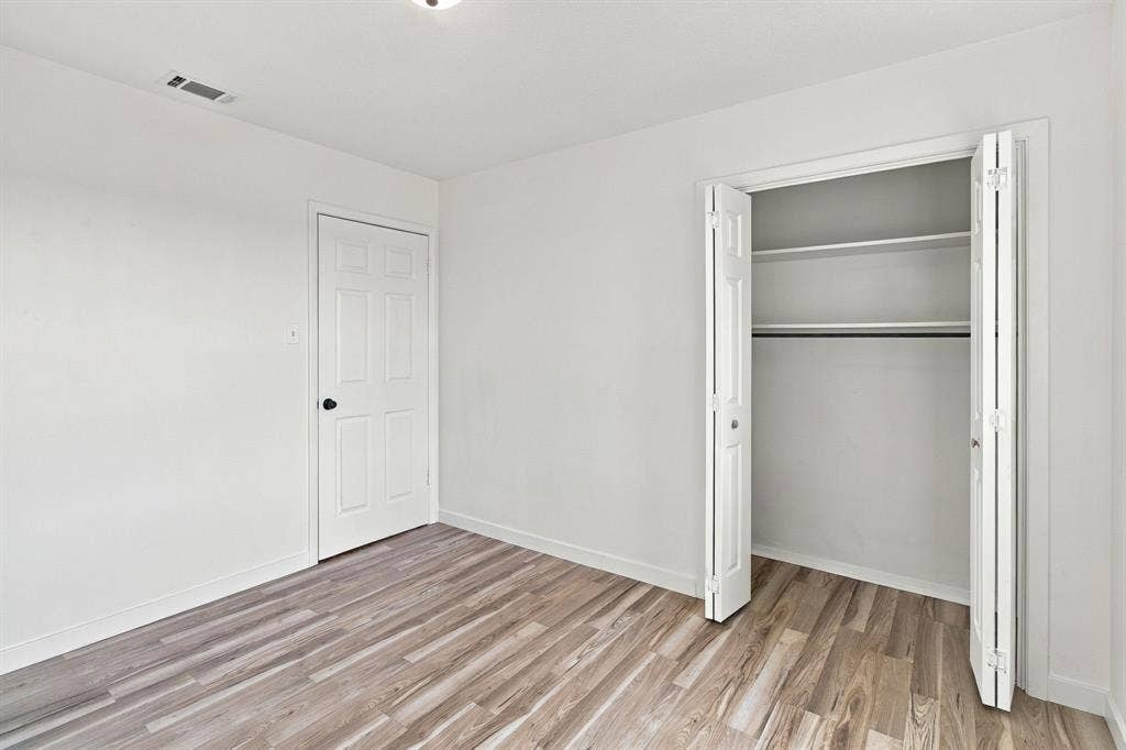 LVP flooring, white walls, white paneled door with black hardware, and a built-in closet with bifold doors and shelving