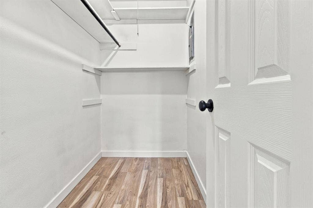Walk-in closet featuring LVP flooring, white painted walls, built-in shelving, and a hanging rod