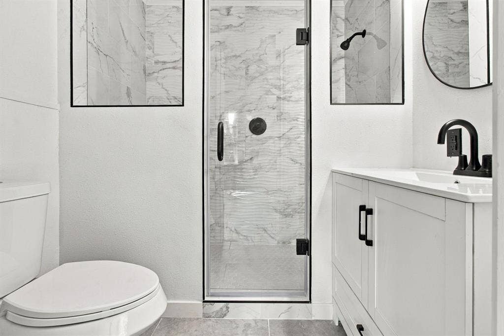 Bathroom featuring a glass-enclosed shower with marble-look wall tile, a single vanity with shaker-style cabinetry, and matte black fixtures