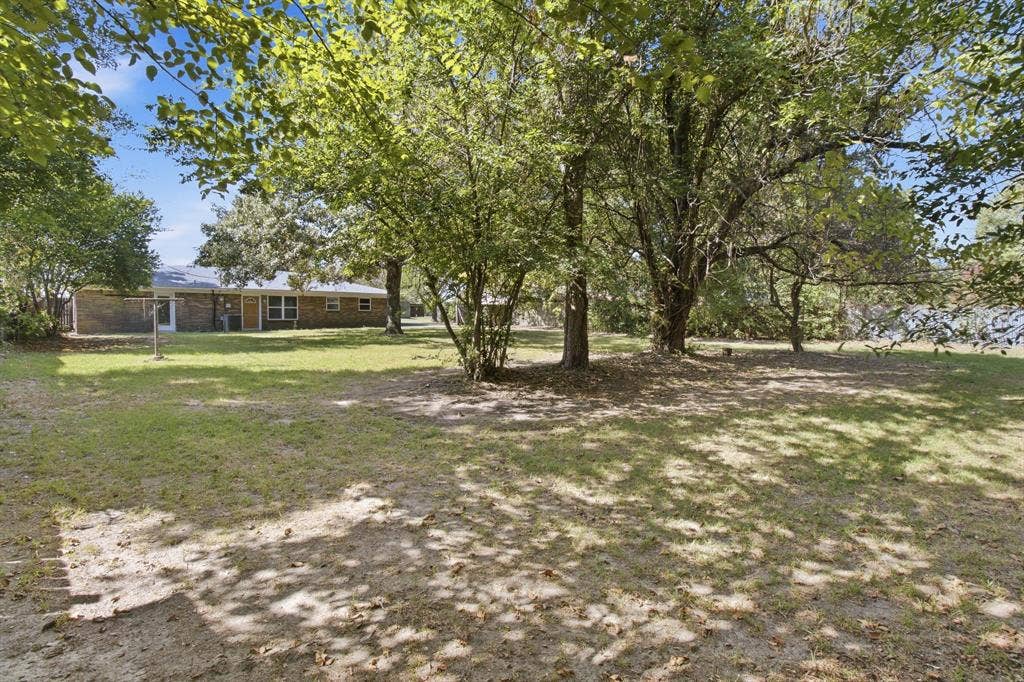 Expansive backyard featuring mature trees, a manicured lawn, and brick exterior