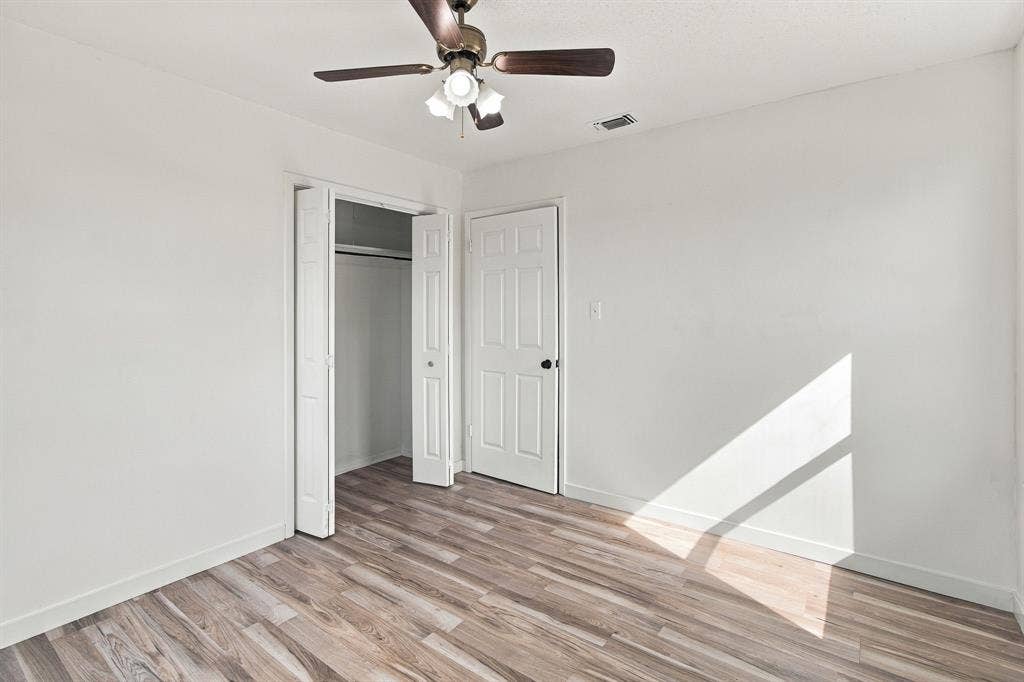 LVP flooring, white walls, ceiling fan with light fixture, white paneled door with black hardware, and bi-fold closet doors