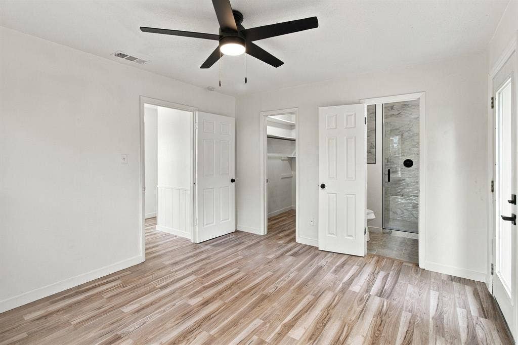 LVP flooring, white walls, black ceiling fan, white paneled doors, and a walk-in closet