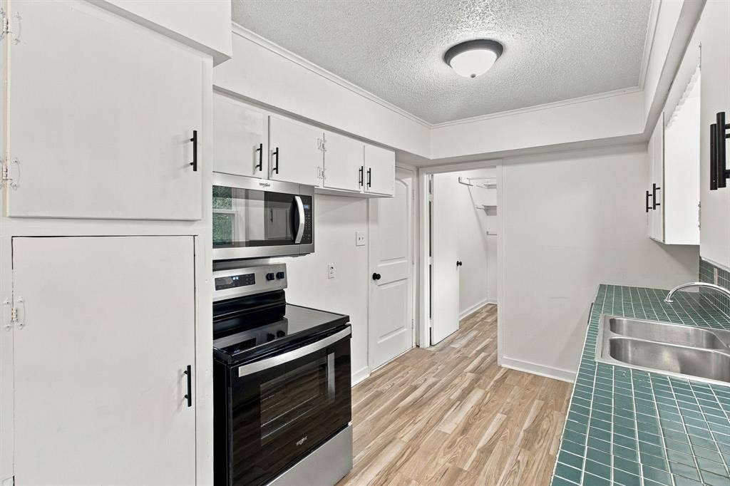 Kitchen featuring white cabinetry, brand new stainless steel appliances, a double basin sink, tile countertops, and wood-finish flooring