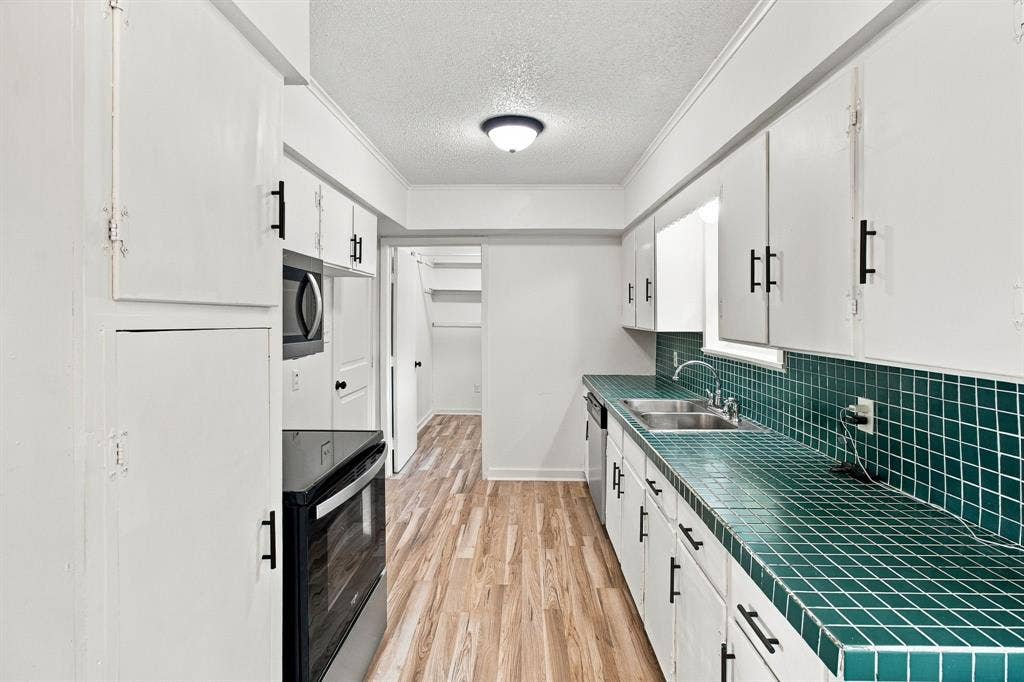 Kitchen featuring wood-finish flooring, white cabinetry with black hardware, integrated microwave, and a double basin sink
