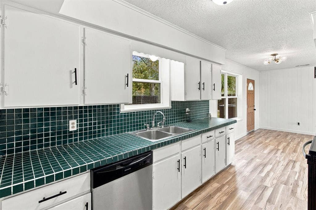 White cabinetry, green tiled countertops, stainless steel double basin sink, dishwasher, and wood-finish flooring