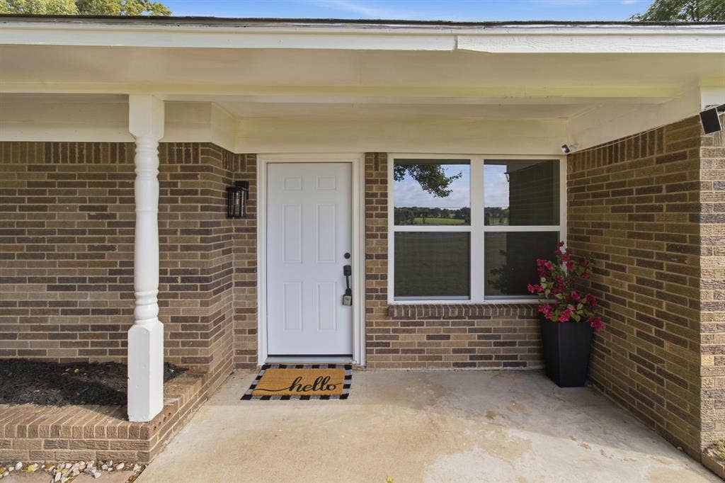 Brick exterior with a covered entry, decorative column, white paneled door, and multi-pane window