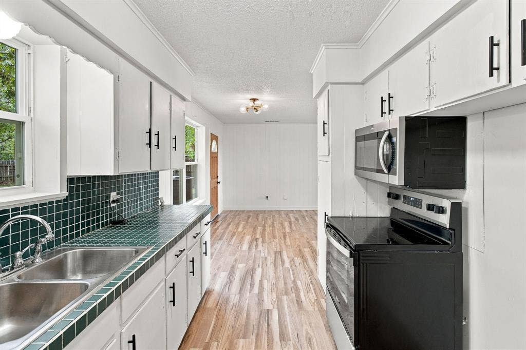 Galley kitchen featuring white cabinetry, dark tile countertops, a double basin stainless steel sink, and wood-finish flooring