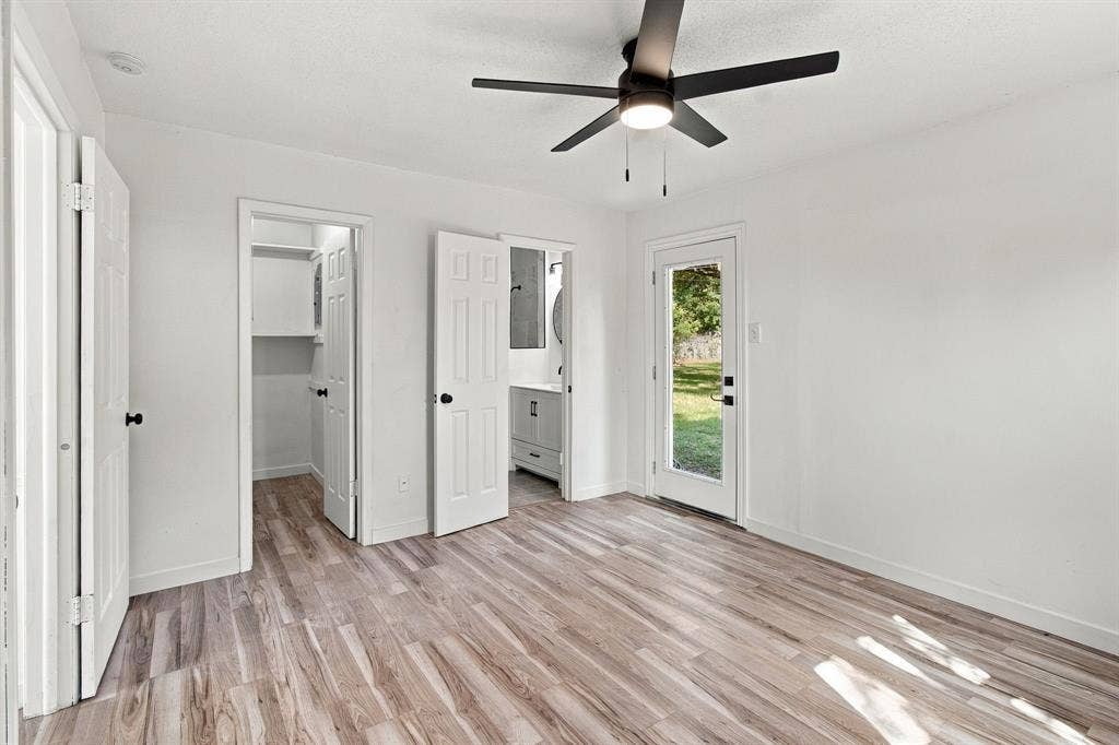 LVP flooring, white walls, black ceiling fan with integrated lighting, built-in closet shelving, and a glass-paneled exterior door