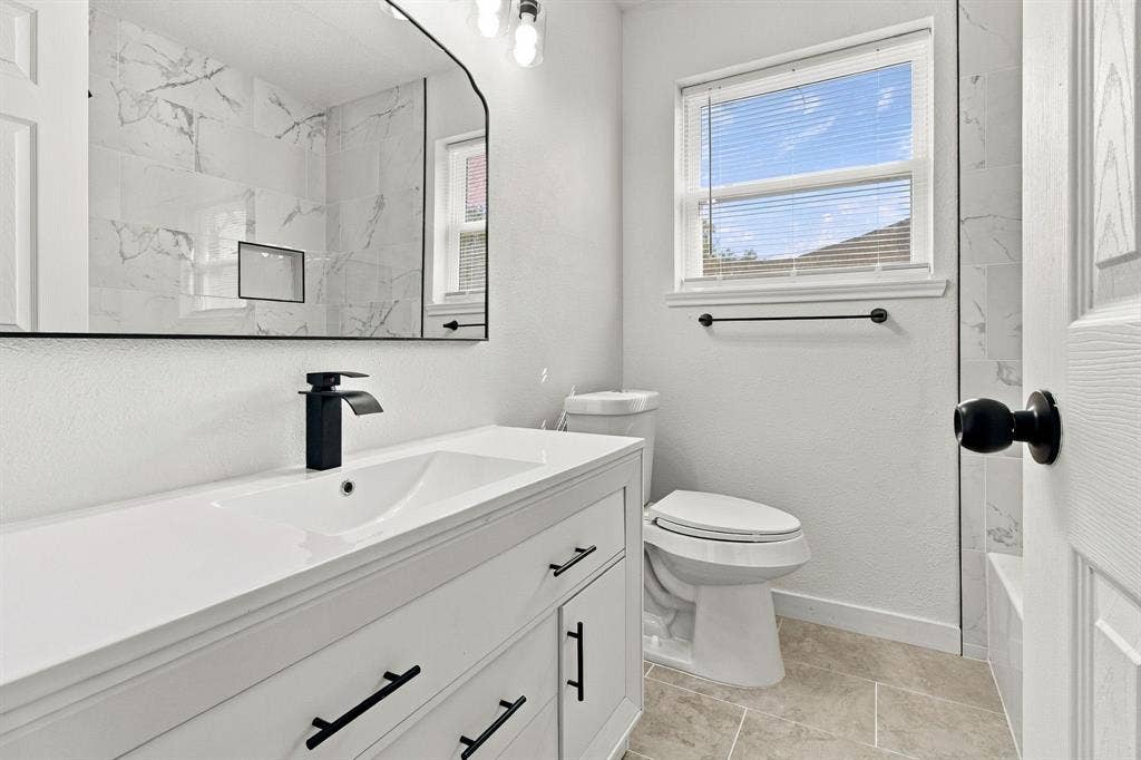 White vanity with matte black hardware, integrated sink, and waterfall faucet