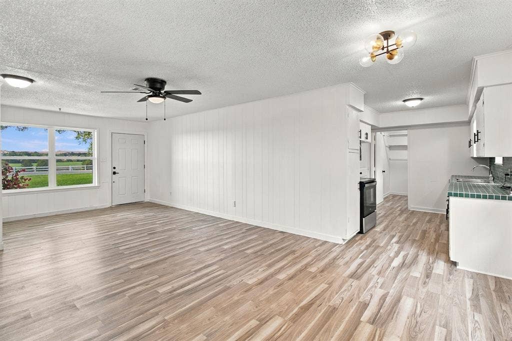 LVP flooring throughout, white walls, modern ceiling fan, contemporary ceiling light fixture, and white cabinetry with dark hardware