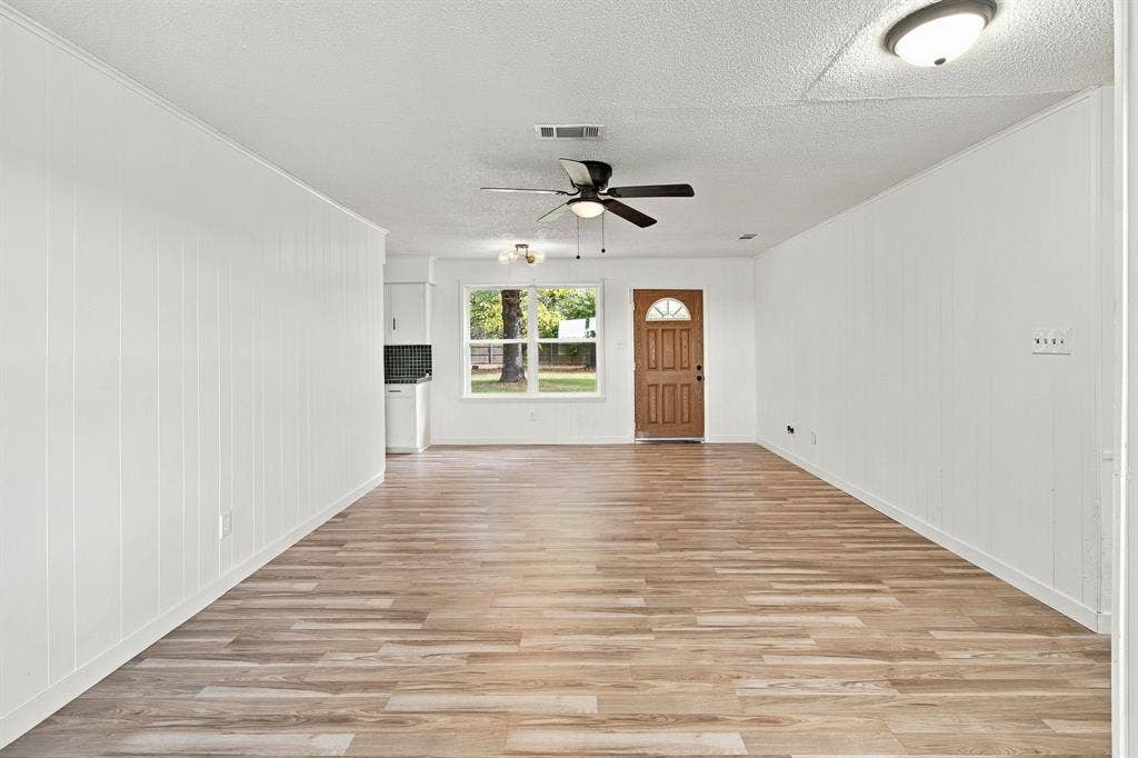 LVP flooring, white panel walls, ceiling fan, natural light from a front window, and a paneled front entry door
