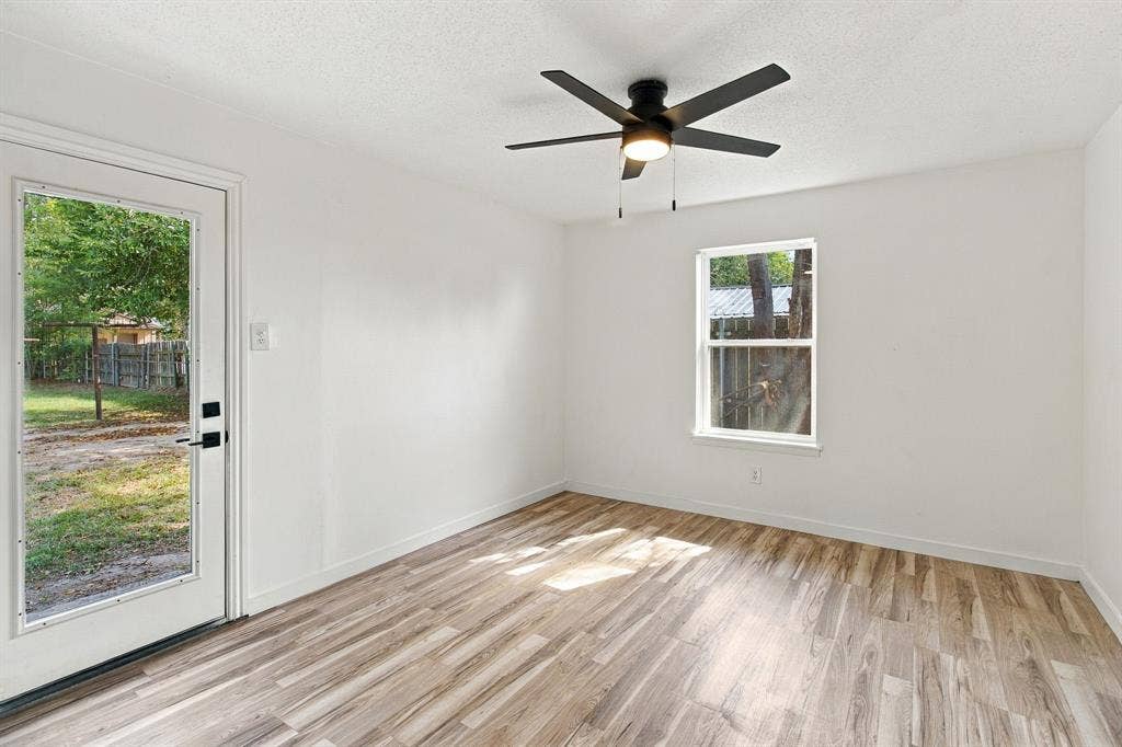Crisp white walls, LVP flooring, black ceiling fan with integrated lighting, and a glass-paneled exterior door