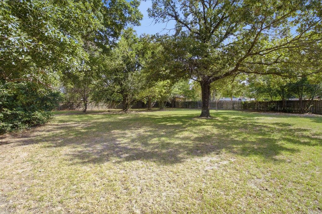 Expansive grass yard with mature trees providing natural shade, enclosed by a wood privacy fence