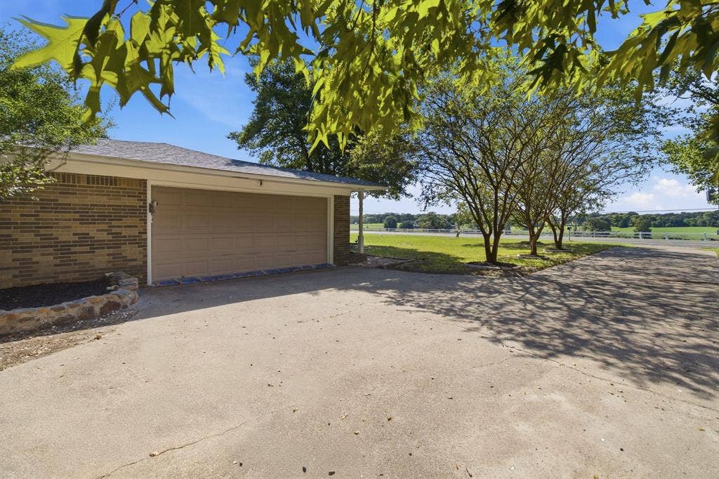 Attached two-car garage with a concrete driveway, brick exterior, and landscaped beds
