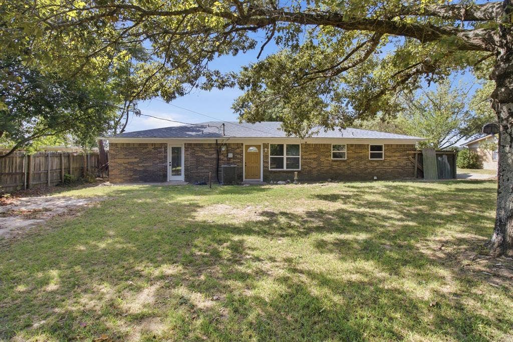 Brick exterior with multiple windows, a rear door with full-length glass, and mature trees providing natural shading