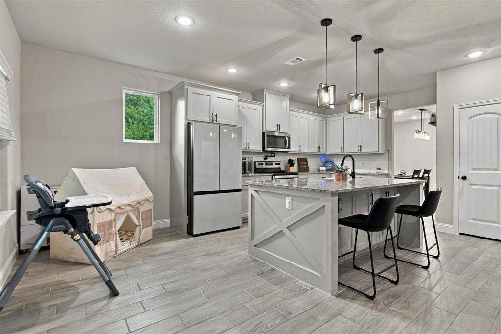 4822 Wichita Street, Granbury, TX 76048 Contemporary kitchen featuring light wood-finish flooring, white cabinetry, stainless steel appliances, a center island with bar seating, and recessed lighting