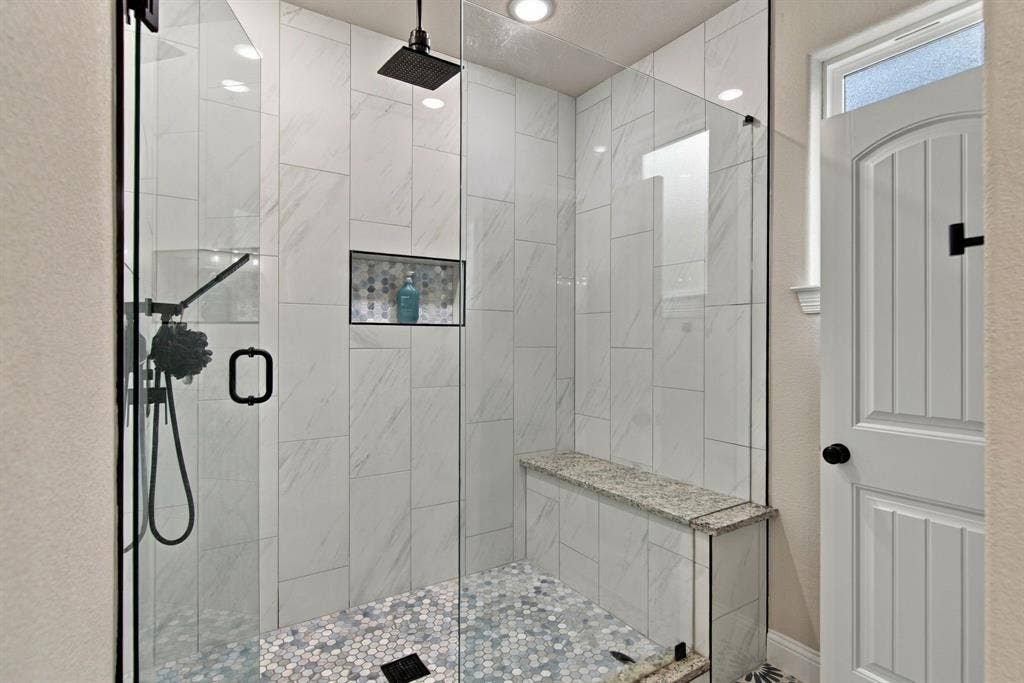 4822 Wichita Street, Granbury, TX 76048 Frameless glass shower enclosure with matte black fixtures, floor-to-ceiling tile, built-in shower bench, and recessed niche