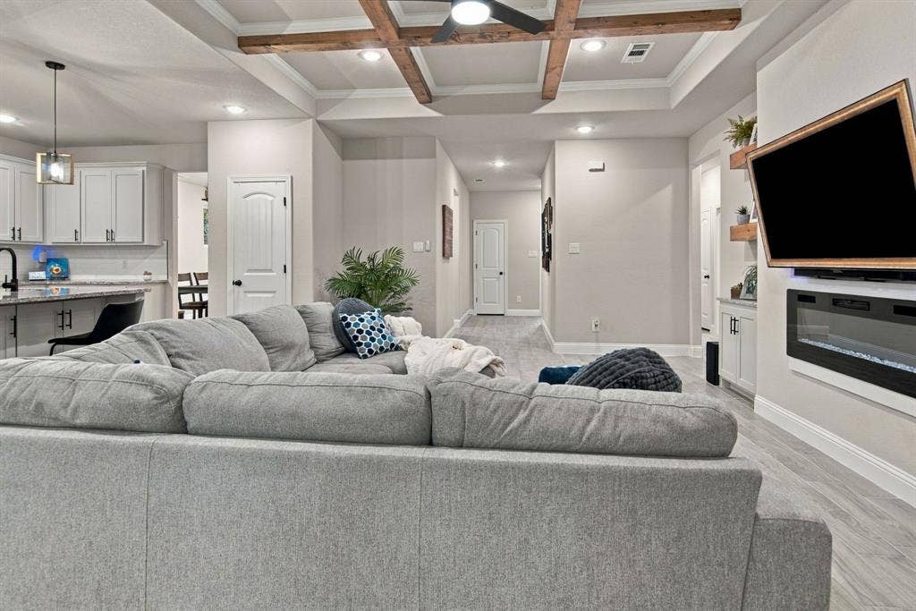 4822 Wichita Street, Granbury, TX 76048 Tray ceiling with exposed wood beams, recessed lighting, wood-finish flooring, built-in electric fireplace, and kitchen with white cabinetry