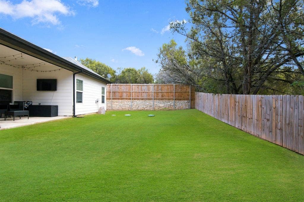 4822 Wichita Street, Granbury, TX 76048 Expansive green lawn with a wood plank fence and a stone retaining wall
