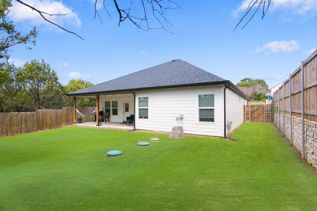 4822 Wichita Street, Granbury, TX 76048 Expansive backyard featuring a covered patio with wood columns, a wood privacy fence, and a stone retaining wall