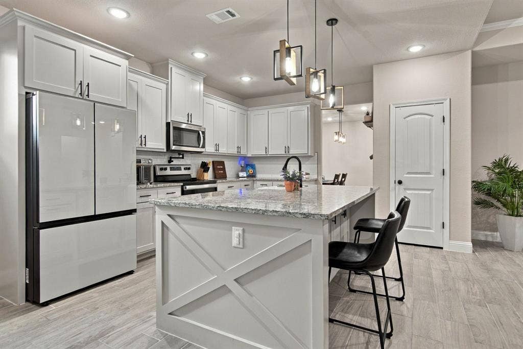 4822 Wichita Street, Granbury, TX 76048 Kitchen featuring white shaker cabinetry, stainless steel appliances, a large island with decorative paneling, pendant lighting, and wood-finish flooring